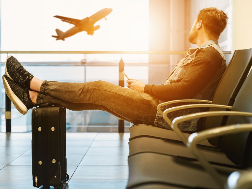 um homem sentado em aeroporto, vendo um avião decolando.
BH é aqui que eu amo